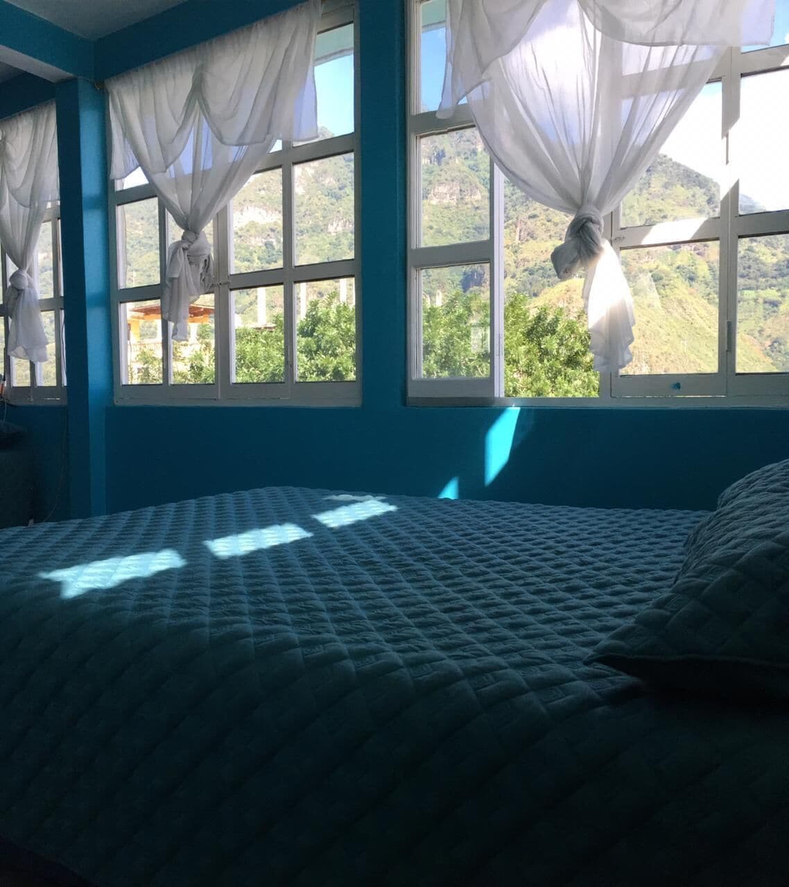 A bedroom with a bed, blue walls, and windows with white curtains.