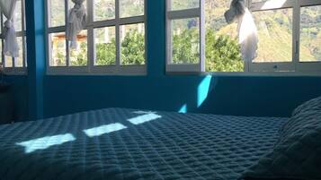 A bedroom with a bed, blue walls, and windows with white curtains.