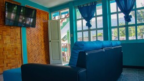 Una habitación con sofá, televisor en la pared y ventana con cortinas.