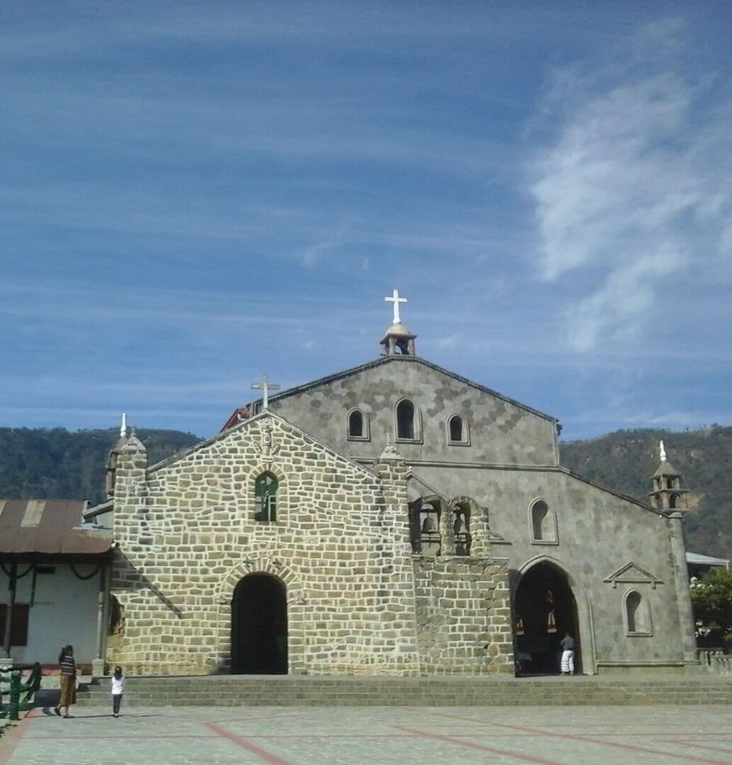 Une église en pierre surmontée d’une croix, dotée d’un clocher et d’une grande entrée en arc de cercle.
