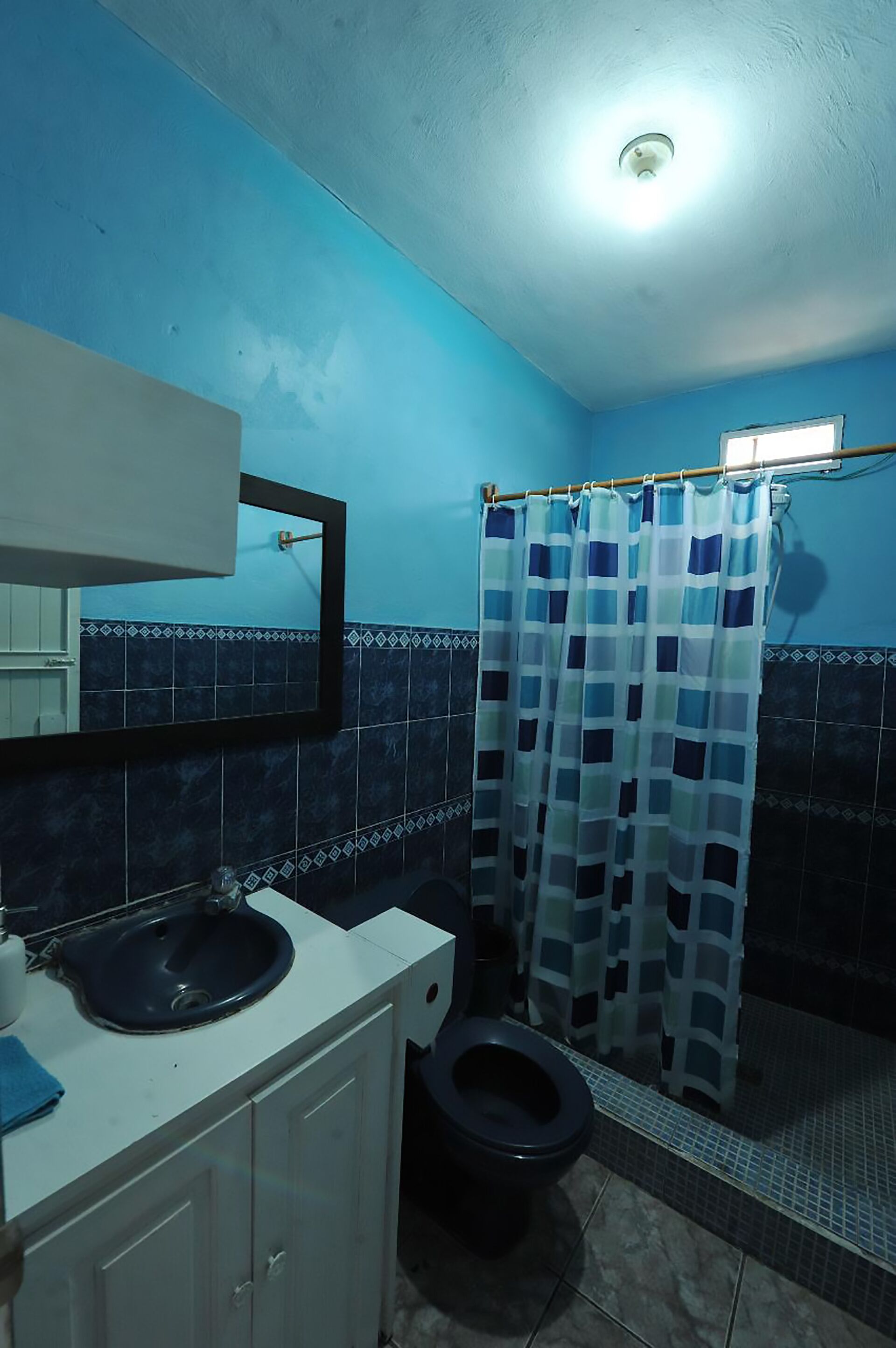 Un baño con cortina de ducha azul y blanca a cuadros, un lavabo blanco y un inodoro negro.