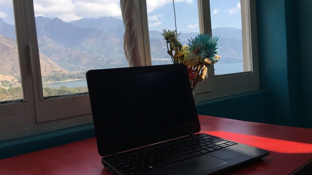 Una computadora portátil sobre un escritorio rojo junto a una ventana con vista a las montañas.