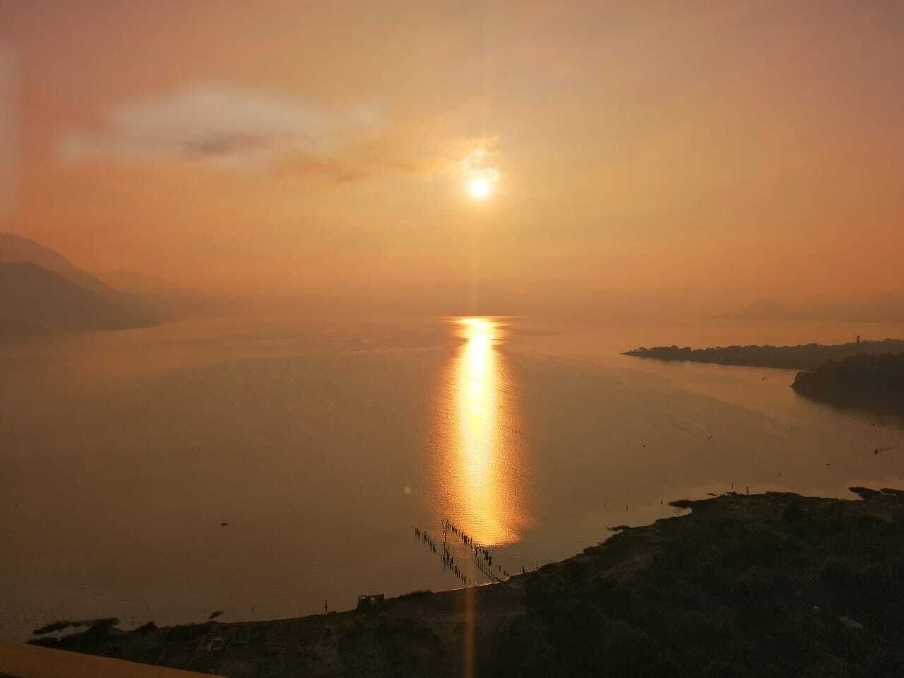 Un atardecer sobre un cuerpo de agua tranquilo, con una costa distante.