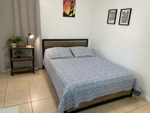 Un dormitori amb un llit, una tauleta de nit amb una làmpada, i una paret amb dos quadres emmarcats.