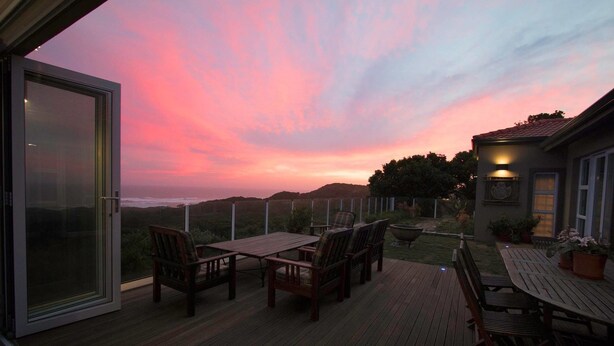 Une terrasse dotée de mobilier d’extérieur, d’une porte vitrée et offrant une vue sur le coucher de soleil sur l’océan.