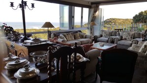 Un salon confortable avec vue sur l’océan, aménagé avec des canapés, une table basse et un coin repas avec de la vaisselle et des couverts.