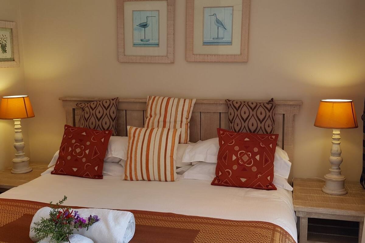 Habitación de hotel con cama, dos lámparas de noche, un cabecero y dos cuadros enmarcados.