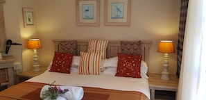 A hotel room with a bed, two bedside lamps, a headboard, and two framed wall art pieces. - Hillscapes (Port Alfred)