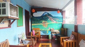 A room with a mural of a mountain and a bird, wooden furniture, a fan, and a table with a box. - J's Backpackers Hostel (Davao)