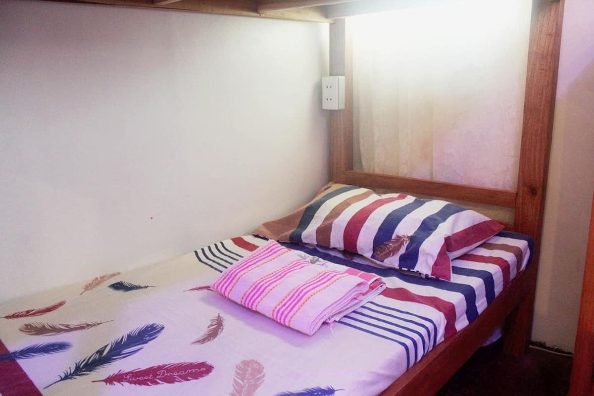 Una cama individual con ropa de cama a rayas, un almohadón, un enchufe de pared y un cabecero de madera.