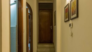 Un couloir au sol recouvert de marbre, une porte en bois au fond et des tableaux encadrés accrochés au mur.