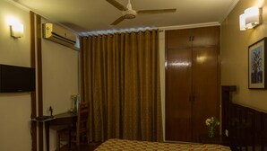 Une chambre d’hôtel équipée d’un lit, d’un bureau, d’une chaise, d’un climatiseur, d’un ventilateur de plafond, d’une armoire et d’un téléviseur fixé au mur.