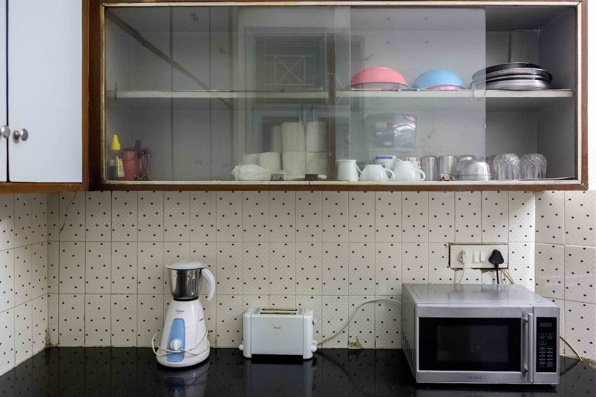Eine Küche mit Mikrowelle, Toaster und Mixer auf der Arbeitsplatte, einem Schrank mit Geschirr und einer gefliesten Spritzschutzwand.