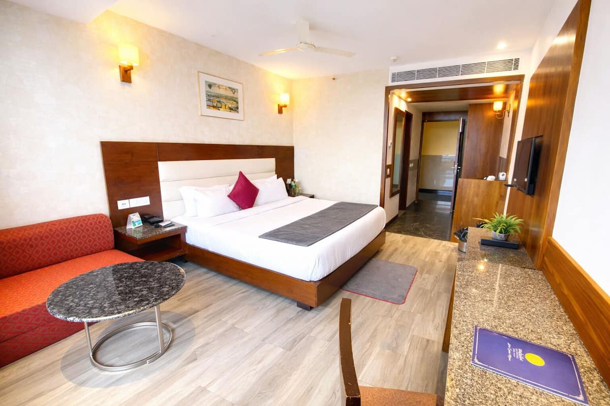 Habitació d'hotel amb un llit, un sofà vermell, una taula rodona petita i una televisió.
