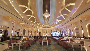 Un'ampia hall d'hotel con un lampadario centrale, diverse zone salotto e un grande schermo che mostra un'immagine.