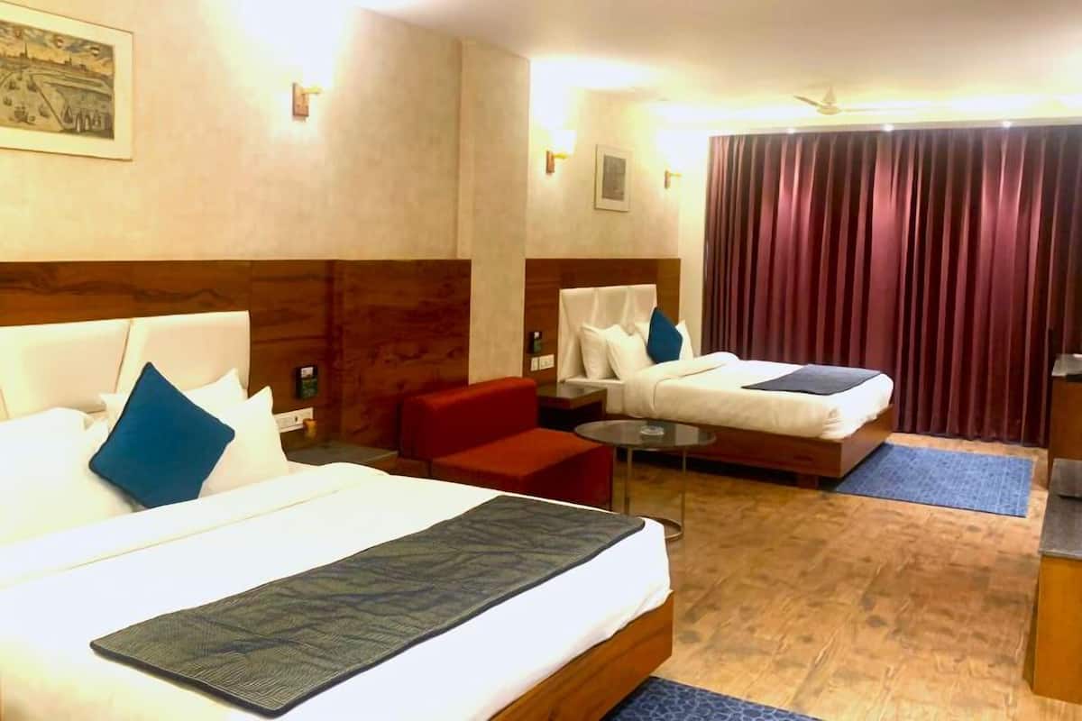 Habitació d'hotel amb dos llits, un sofà vermell, una taula petita i un ventilador de sostre.