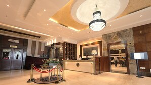 A hotel reception area with a marble floor, a reception desk, a chandelier, and a CCTV monitor.