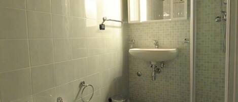 Et badeværelse med træloft, toiletbidét, vask og bruser.