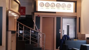 Un hall d’hôtel avec un escalier, un espace salon et un mur où sont exposées des horloges indiquant l’heure de différentes villes.