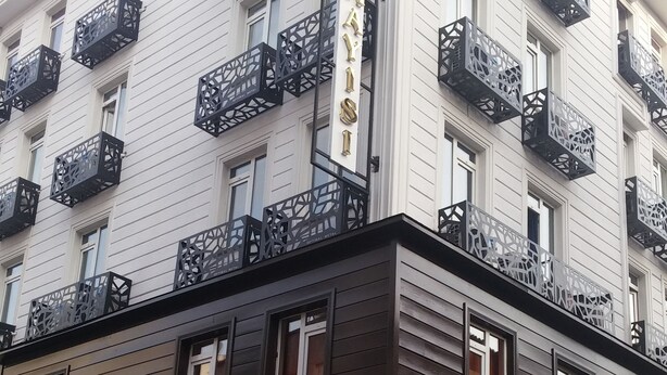 Un hôtel avec une enseigne indiquant « HÔTEL KAWISI » et des balcons ornés de garde-corps en métal aux motifs complexes.