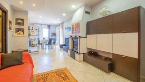 A modern living room with a sofa, a coffee table, and a fireplace. There is a dining area with chairs and a table. The kitchen has cabinets and a stove. - 3 bedroom nice apartment in Bari (Bari)