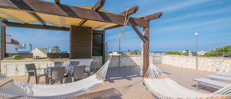 A rooftop terrace with a wooden pergola, outdoor seating, and hammocks.