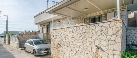 A modern building with a stone facade, a covered parking area, and a parked car.