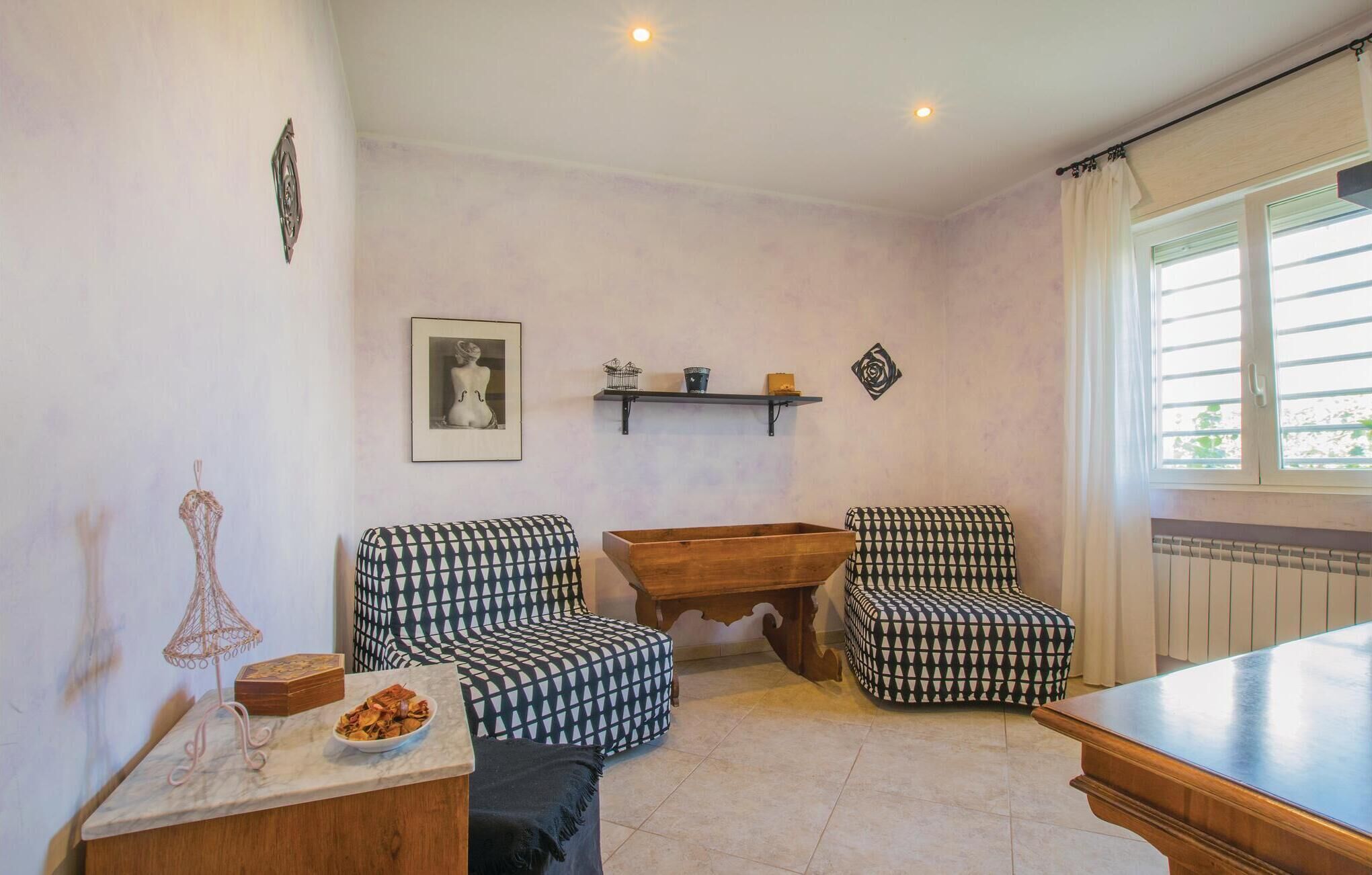 A room with two patterned armchairs, a wooden coffee table, a marble side table with a bowl of snacks, a framed picture on the wall, and a window with curtains.