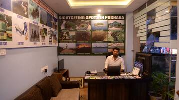 A reception desk with a large poster of sightseeing spots in Pokhara, a man sitting behind the desk, and a couch to the left.
