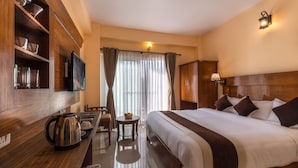 A hotel room with a large bed, wooden headboard, a coffee table, a chair, a television, and a window with curtains. - Hotel Lake Shore (Pokhara)
