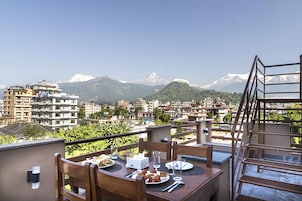 Un comedor con una mesa dispuesta para dos personas, con vistas a un paisaje montañoso y edificios al fondo.