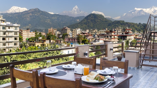 A dining table set with plates, cutlery, and a glass of orange juice, overlooking a cityscape with mountains in the background. - Hotel Lake Shore (Pokhara)
