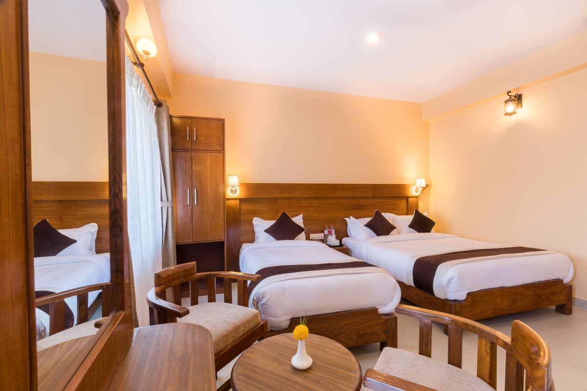 A hotel room with three beds, wooden furniture, and wall-mounted lights.