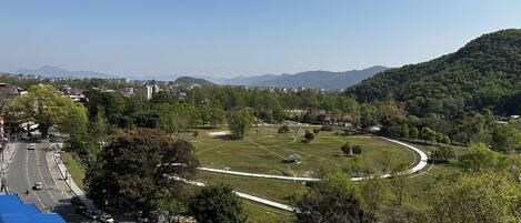A park with a circular walking path, surrounded by trees and a hilly landscape.