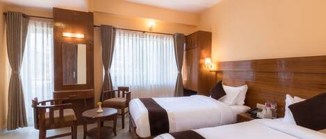 A hotel room with two beds, a desk, a chair, and a mirror.