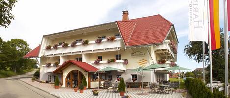 A hotel with a red roof, multiple balconies with flower boxes, outdoor seating, and a tiled patio.