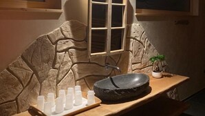Un baño con pared de piedra, un banco de madera, un lavamanos y un ventanal.
