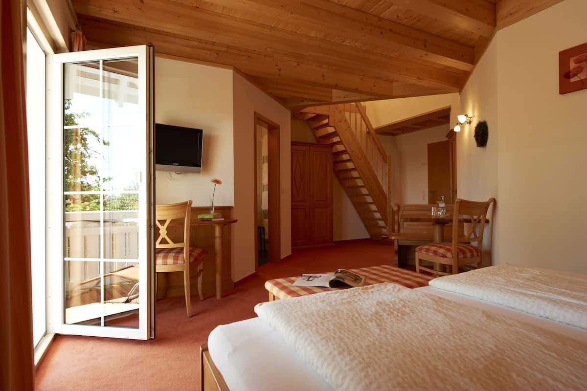 Une chambre avec un plafond en bois, un lit, un bureau avec une chaise, une télévision et un escalier menant à une autre pièce.