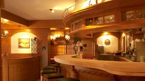 Zona de bar con mostrador y taburetes de madera, un reloj y una estantería para vinos.