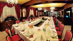 Une salle à manger élégante, avec de longues tables dressées pour le repas, des chaises à revêtement rouge et des lustres.