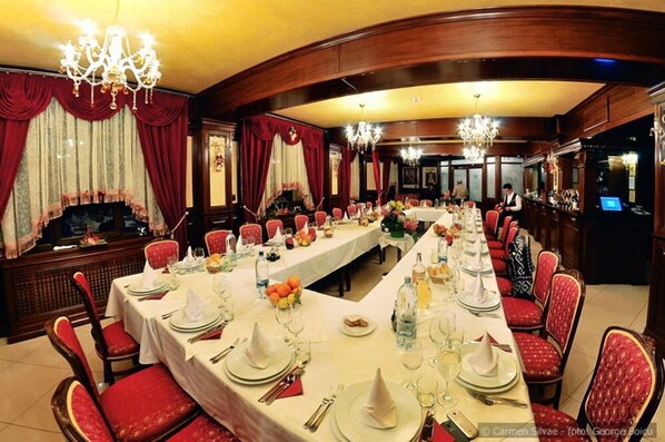 A formal dining room with long tables set for a meal, red upholstered chairs, and chandeliers. - Vila Turistica Carmen Silvae (Gura Humorului)