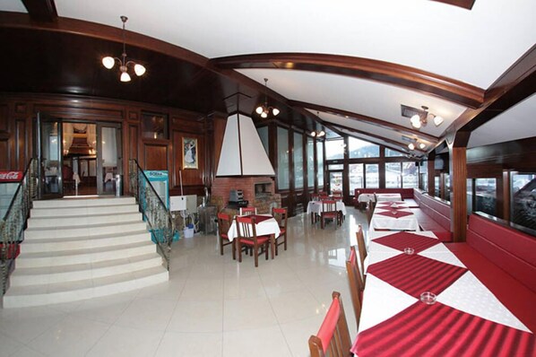 Un restaurante con una escalera que lleva a un área de bar, ventanas amplias y un techo alto con vigas a la vista.