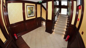 Un couloir avec un plancher en bois, un escalier et un extincteur sur le côté gauche.