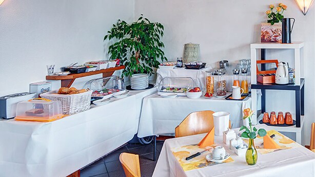 A breakfast buffet setup with various food items, a plant, and a coffee station. - Hotel Post Rosbach (Rosbach vor der Hoehe)