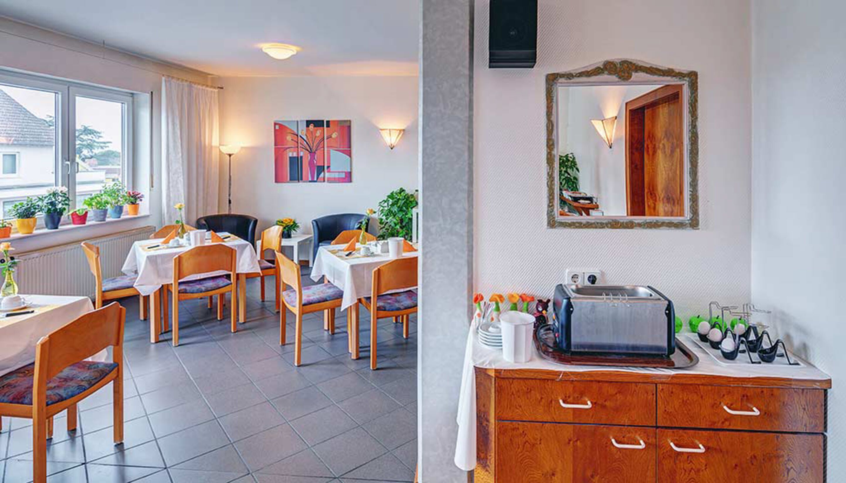 A dining area with tables and chairs, a buffet station with a toaster, and a large window with curtains.