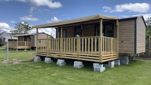 Une cabane en bois dotée d’un balcon, entourée d’herbe et d’autres cabanes.
