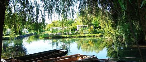 A serene riverside scene with boats docked along the water's edge, surrounded by lush greenery and trees.