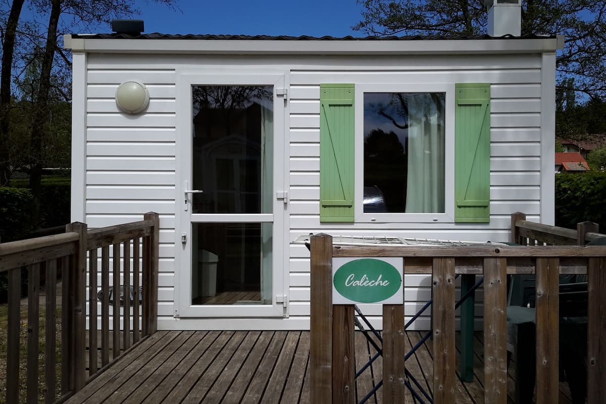 Un pequeño edificio blanco con contraventanas verdes, una terraza de madera y un letrero que dice