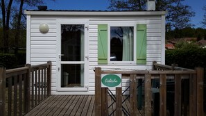 Un pequeño edificio blanco con contraventanas verdes, una terraza de madera y un letrero que dice