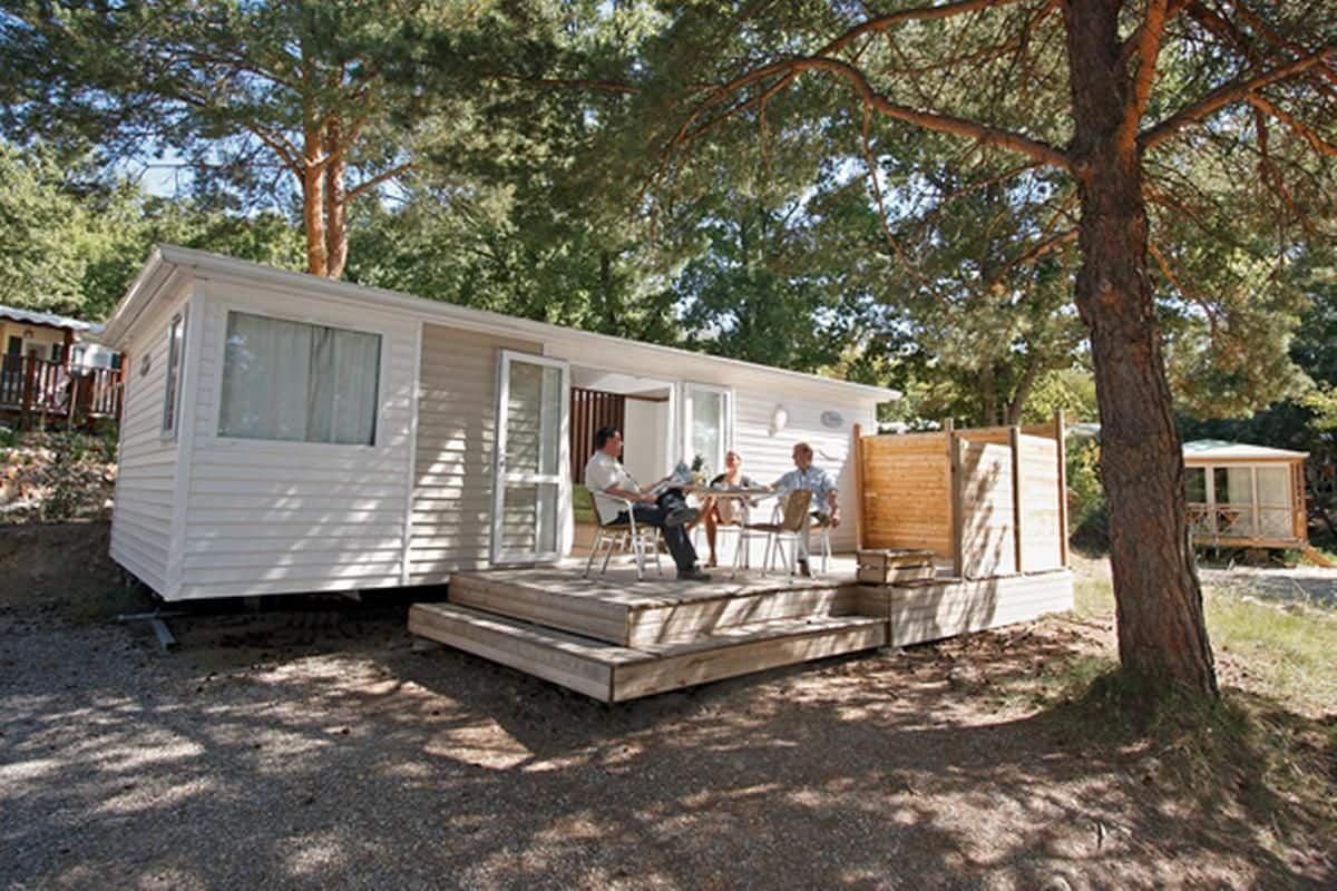 A mobile home with a porch and a small deck, surrounded by trees.